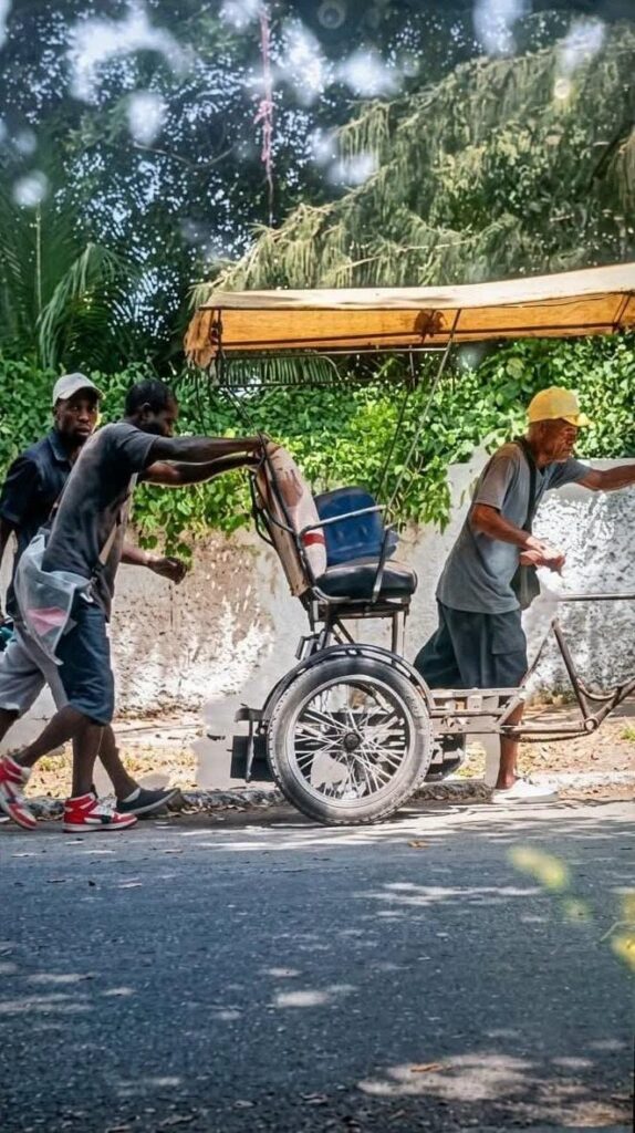 Tres hombres empujando un bicitaxi en una calle soleada.