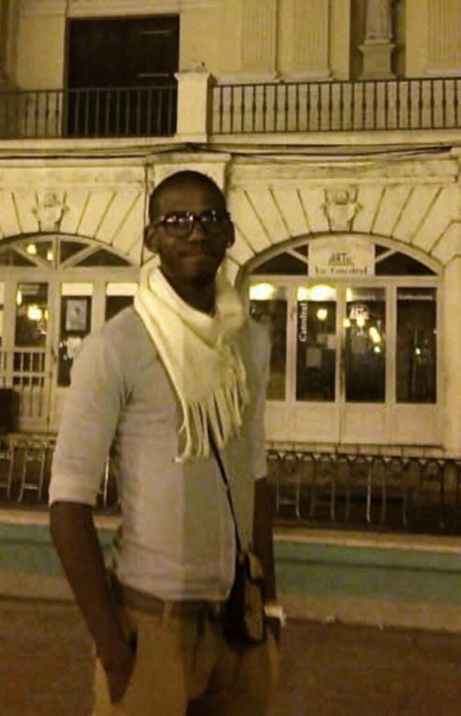 Hombre joven con bufanda blanca ante un edificio iluminado.