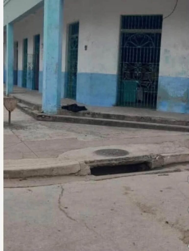 Fachada de edificio azul y blanco con alcantarilla abierta.
