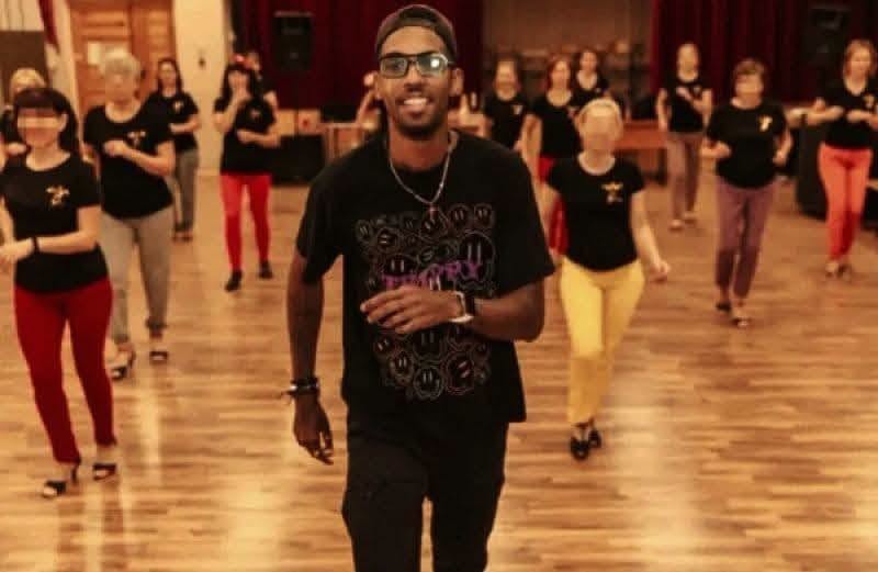 Hombre sonriente dirigiendo una clase de baile grupal.
