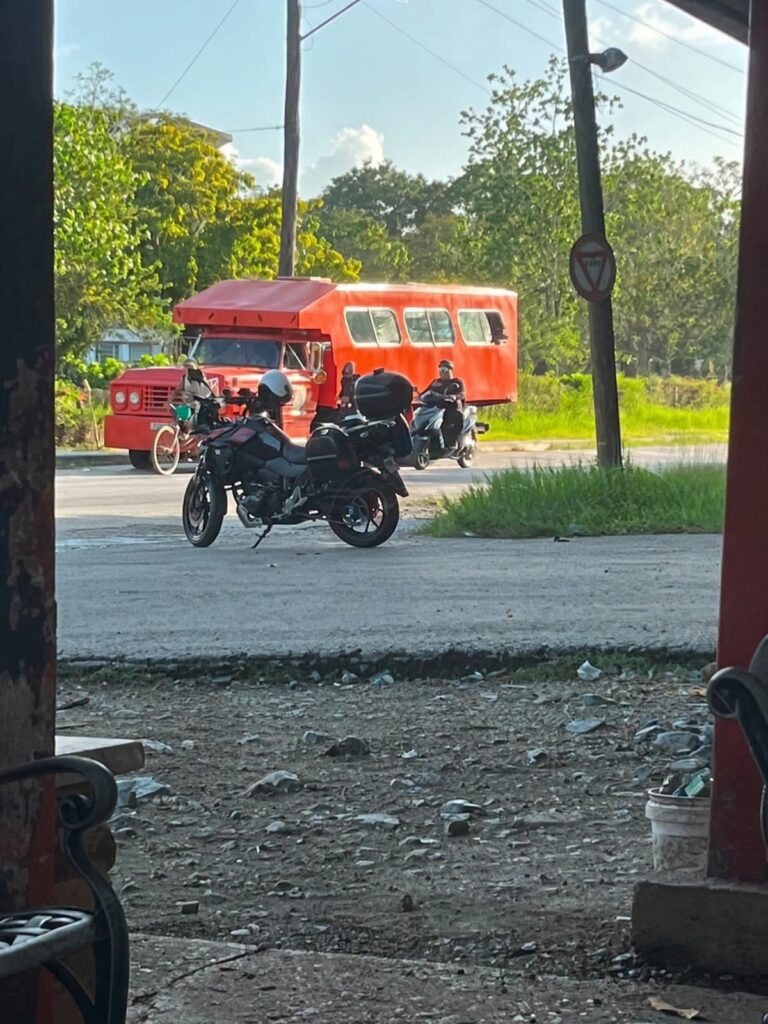 Motocicleta negra aparcada frente a un autobús rojo artesanal.