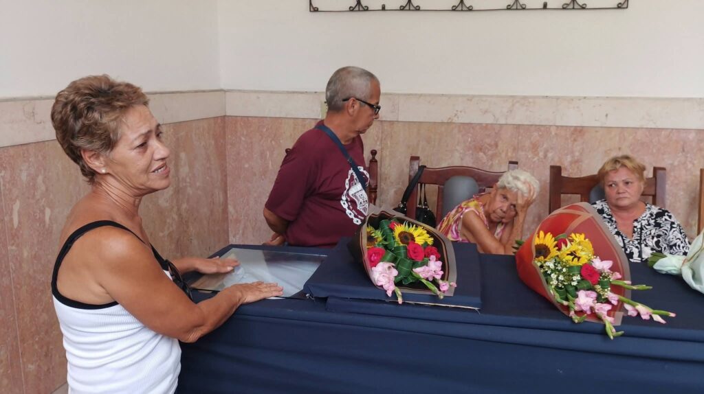 Mujer llorando junto a un féretro con flores.