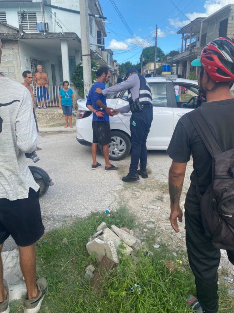 Policía arrestando a un hombre esposado junto a patrulla blanca.