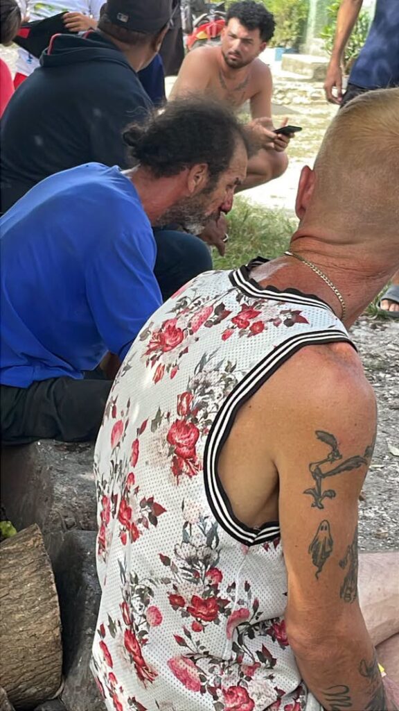 Hombre con camiseta de flores y tatuajes sentado al aire libre.