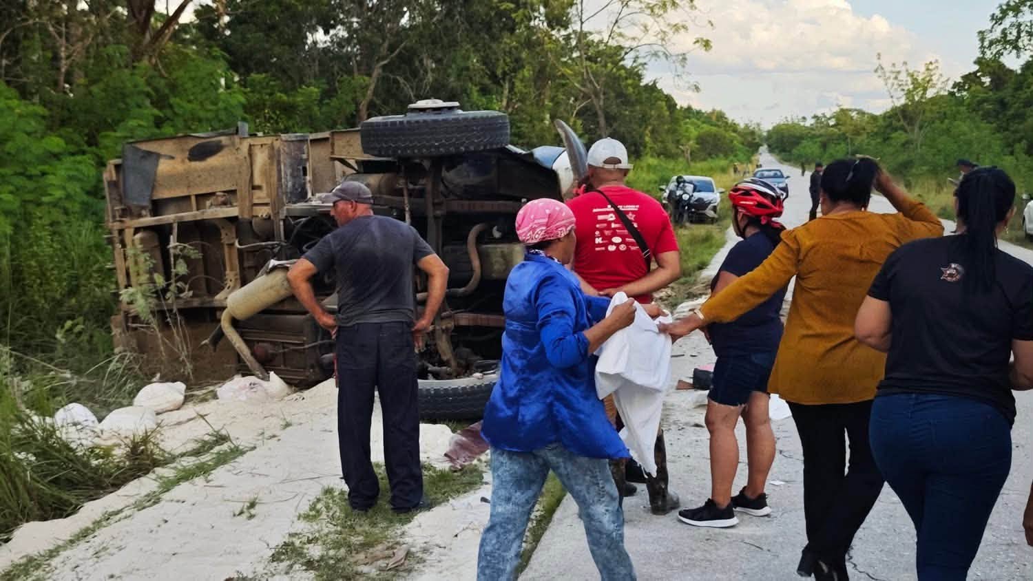 Camión volcado en una carretera rural con personas alrededor.