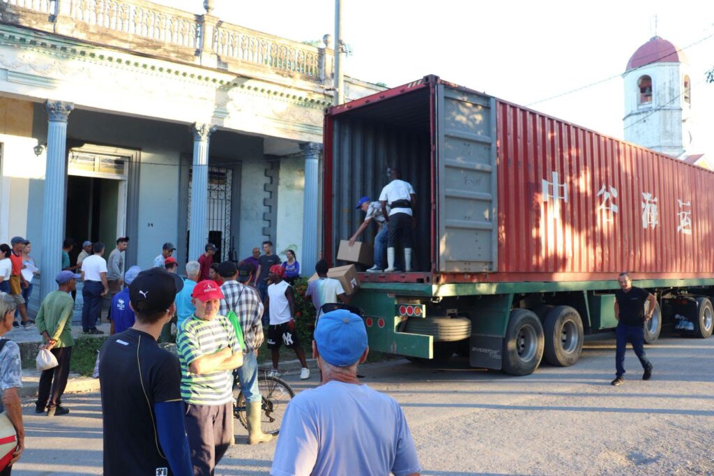 Personas descargando cajas de un gran contenedor de carga rojo.