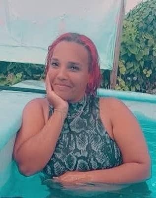 Mujer con pelo rosa sonriendo en una piscina exterior.