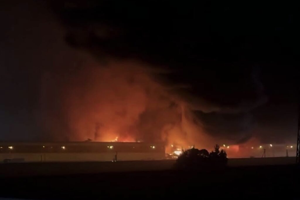 Gran incendio nocturno en un edificio industrial con humo denso.