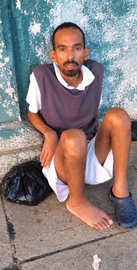 Hombre sentado en el suelo contra una pared azul desgastada.
