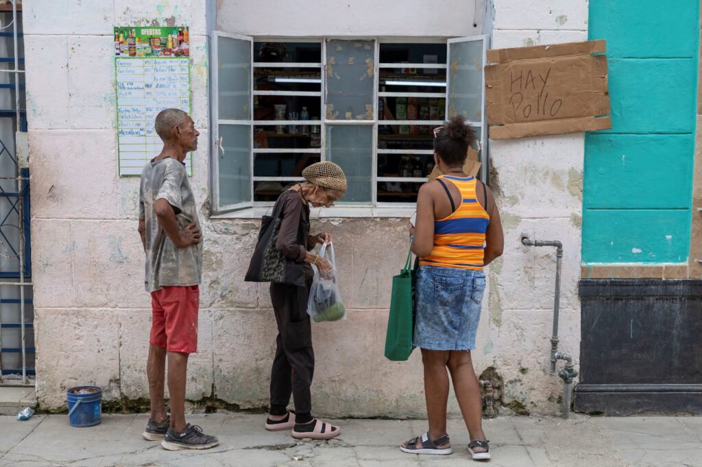 Personas esperando frente a una tienda con cartel "Hay Pollo".