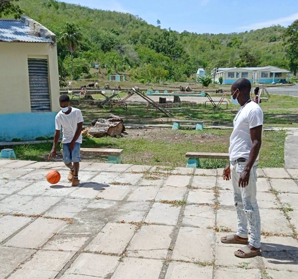 Dos hombres con mascarilla jugando al baloncesto al aire libre.