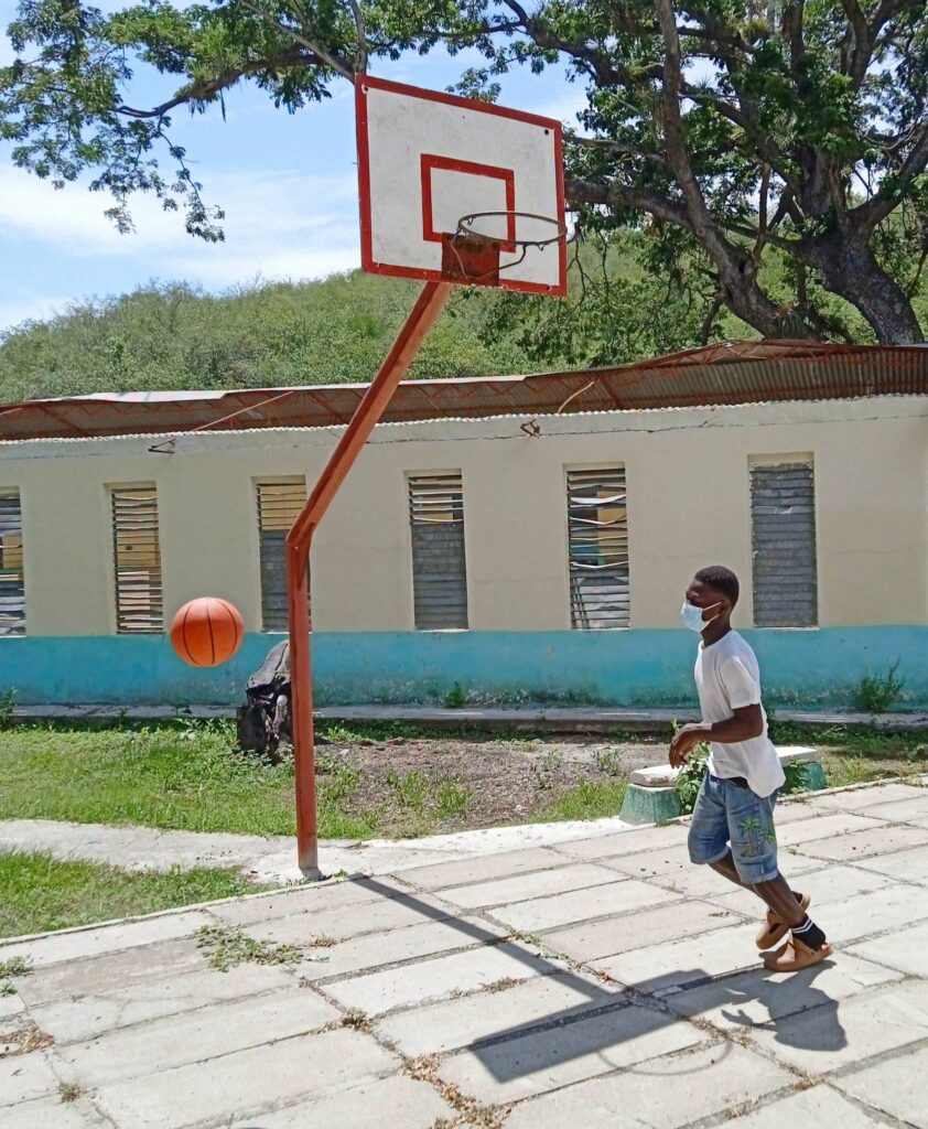 Joven con mascarilla jugando al baloncesto en una cancha exterior.