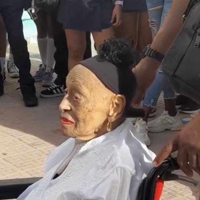Anciana en silla de ruedas con blusa blanca y cinta.
