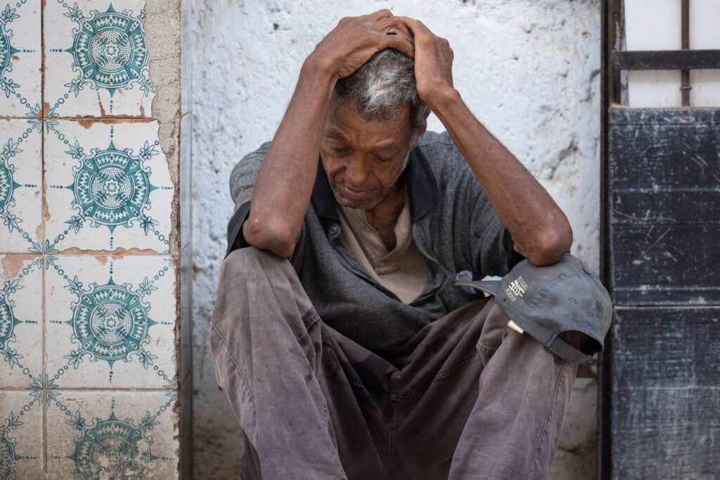 Hombre mayor desolado sentado en el suelo contra una pared.