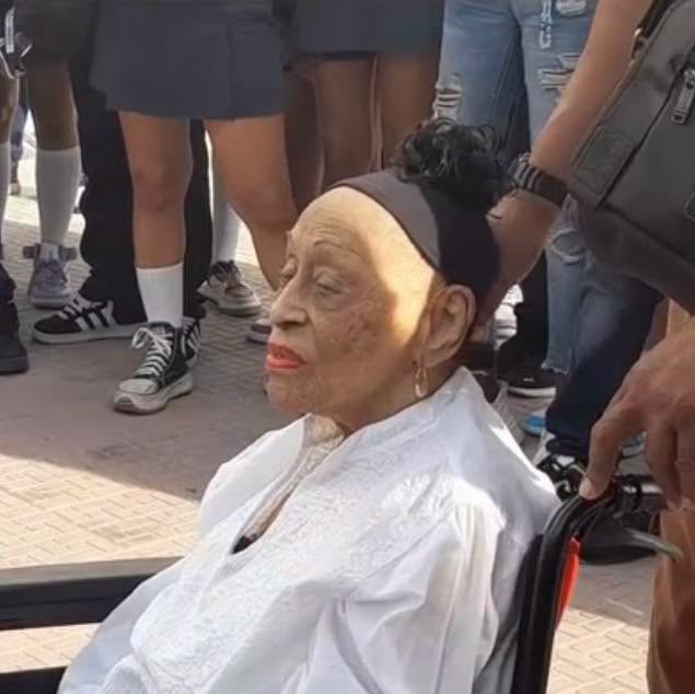 Mujer de avanzada edad en silla de ruedas entre jóvenes.