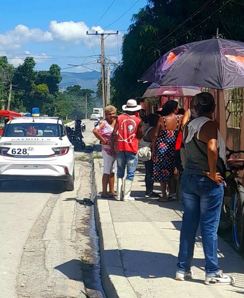 Personas agrupadas en la acera junto a un coche policial.