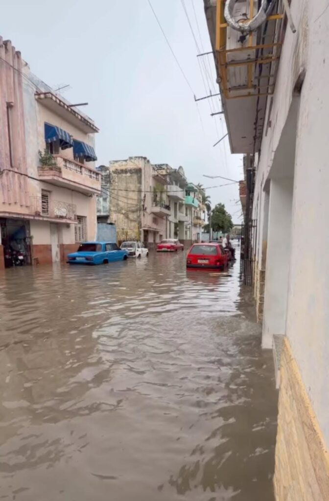 Calle inundada con coches sumergidos y edificios antiguos al fondo.