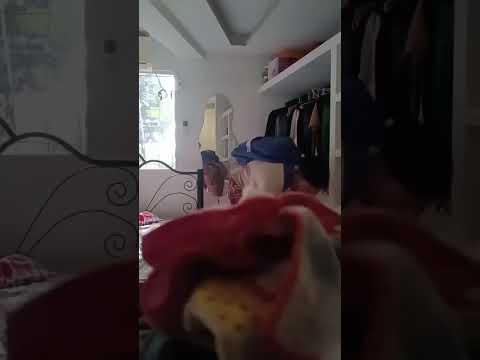 Persona moviendo una prenda roja en un dormitorio iluminado.