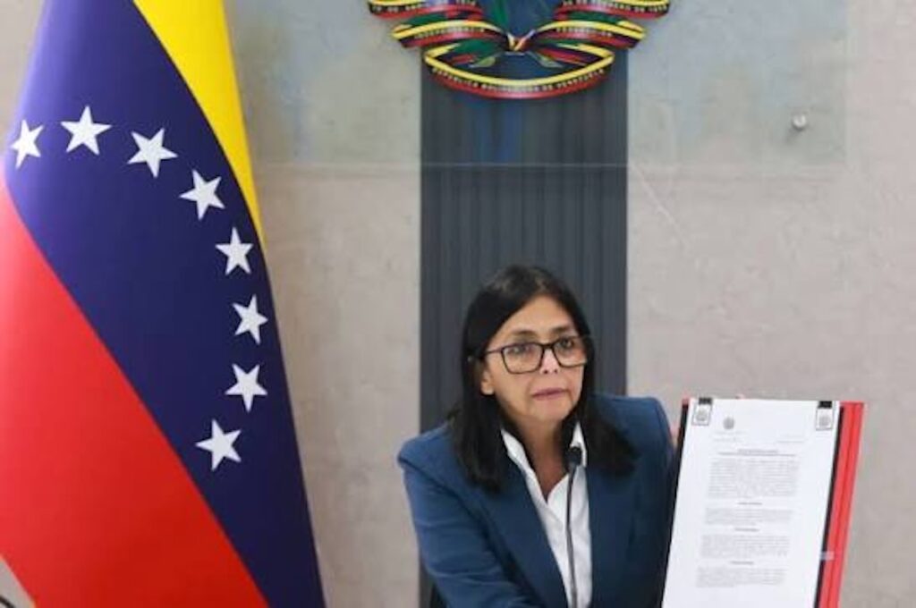Delcy Rodríguez sosteniendo un documento oficial junto a bandera venezolana.