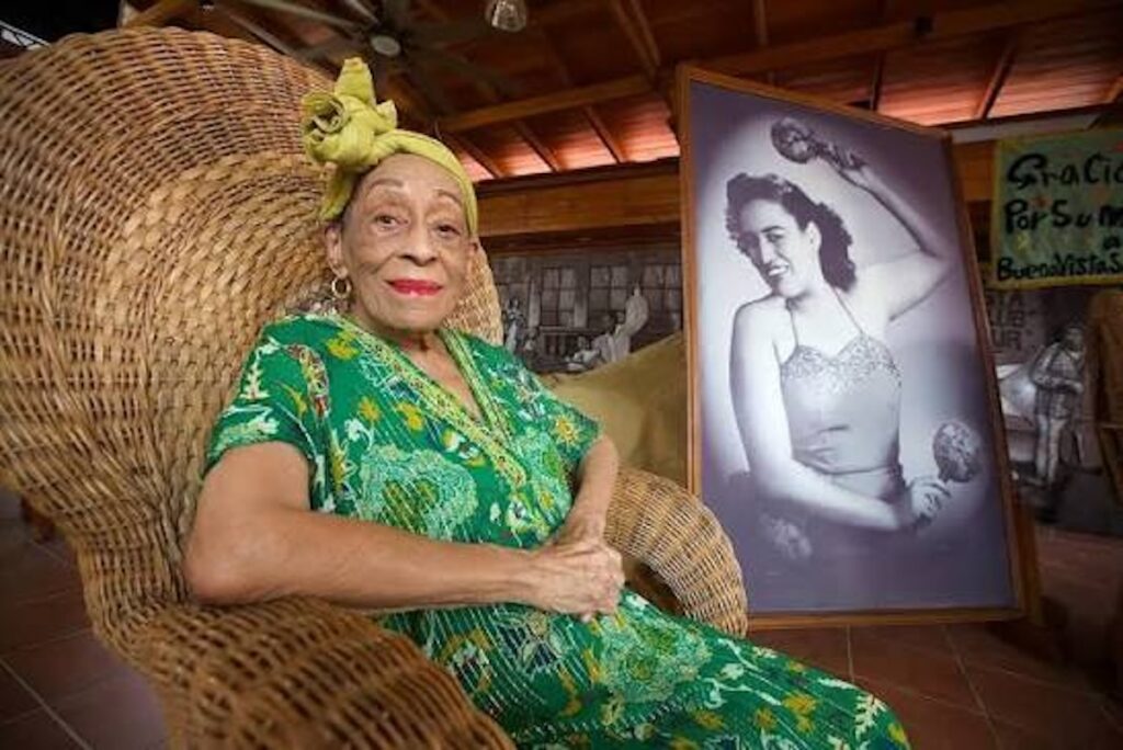 Omara Portuondo sentada en un sillón junto a su retrato.