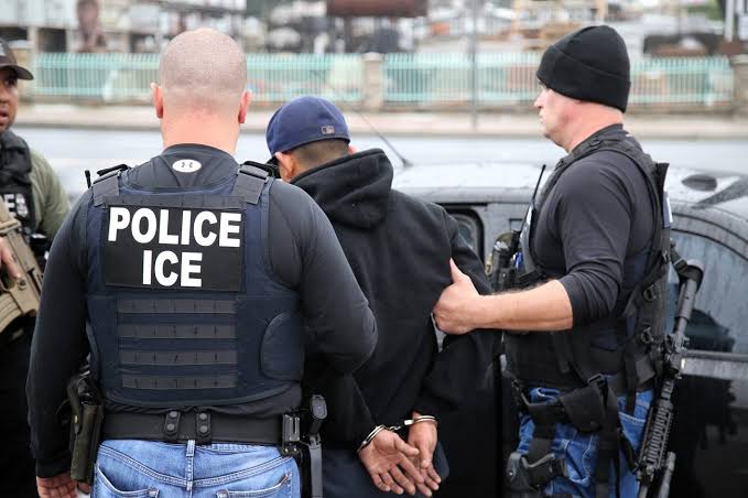 Agentes de ICE deteniendo a un hombre esposado en la calle.