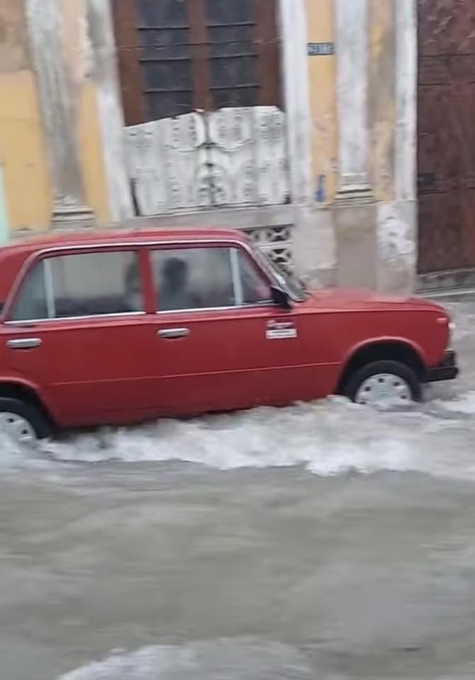 Coche rojo clásico conduciendo por una calle inundada en la ciudad.