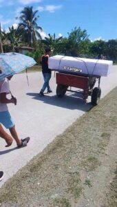 Hombre transportando un ataúd blanco en un pequeño carro motorizado.