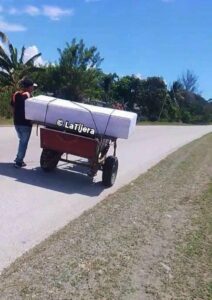 Hombre transportando un ataúd blanco en un carro artesanal.