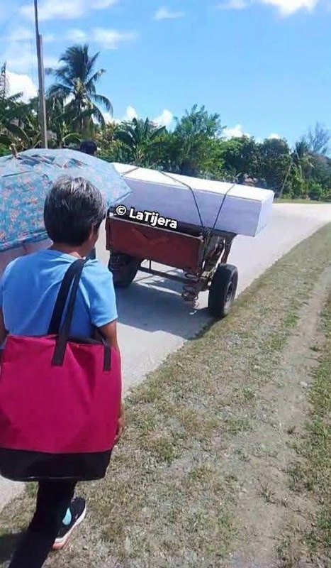 Persona caminando tras un carrito que transporta un ataúd blanco.