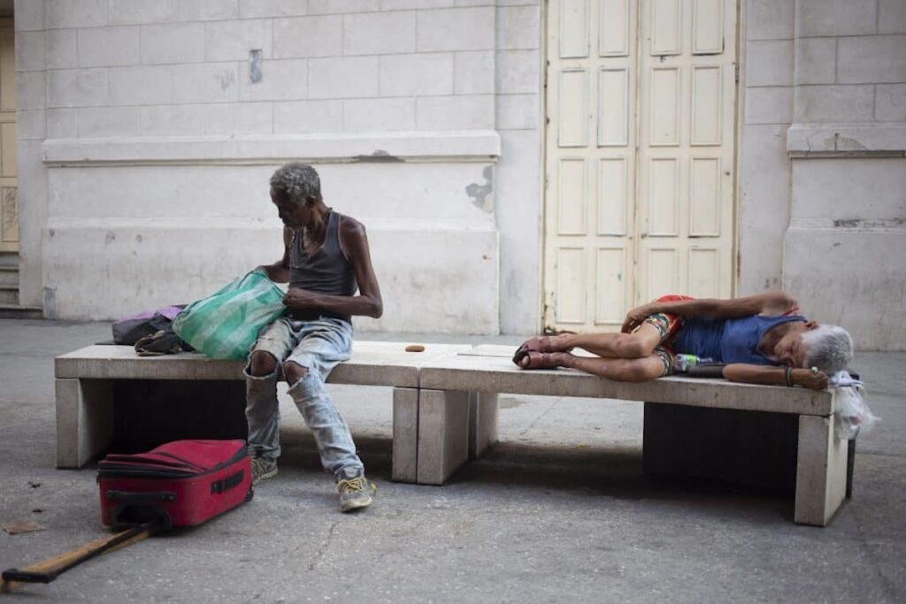 Dos personas descansando en bancos de piedra con sus pertenencias.