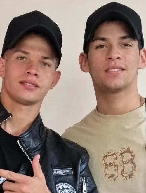 Dos jóvenes con gorras negras sonriendo a la cámara.