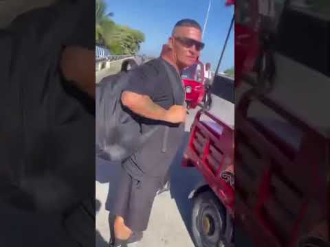 Hombre con mochila negra junto a un motocarro rojo.
