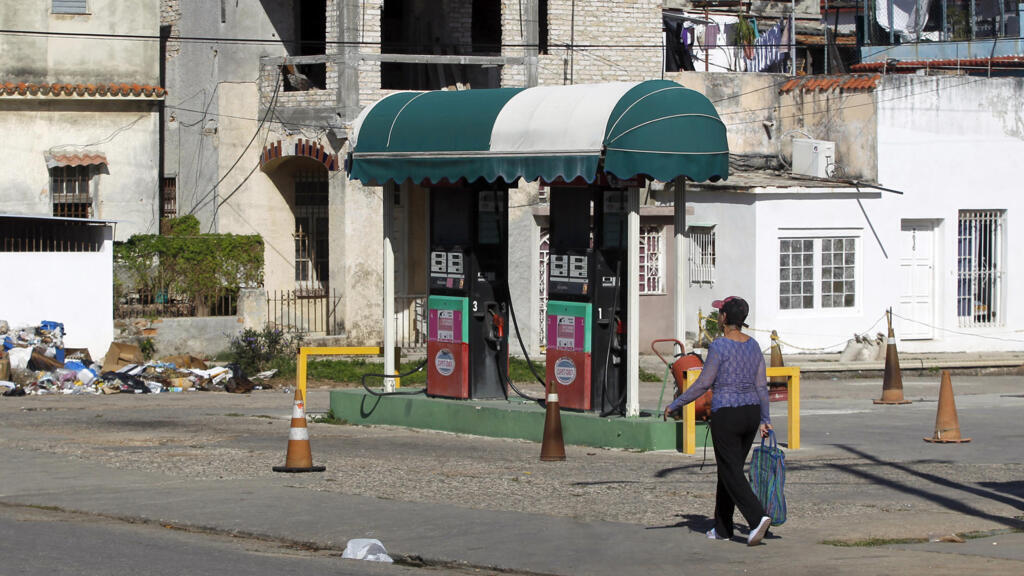 Surtidores de gasolina antiguos bajo un toldo con mujer caminando.